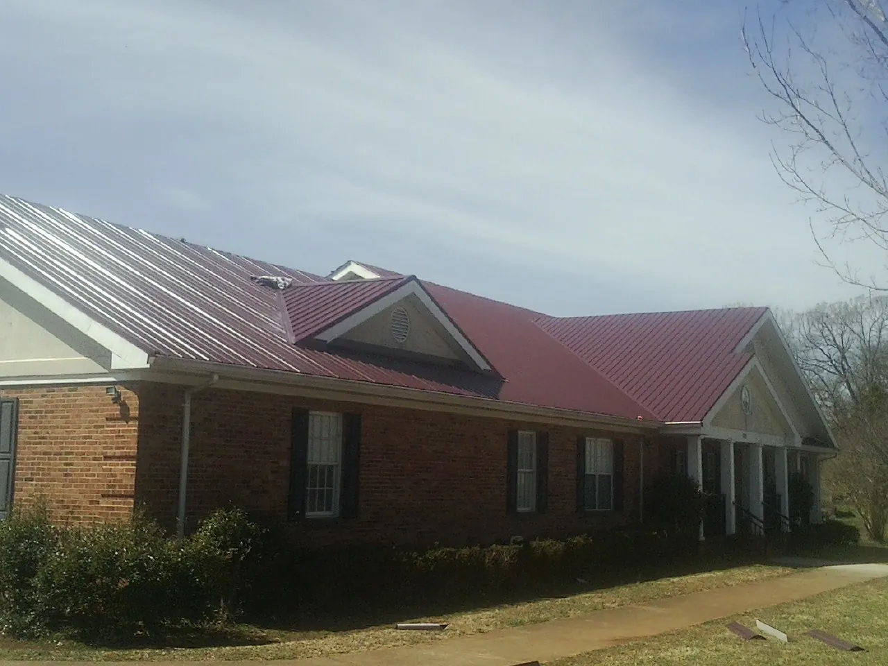 Red metal roof with gabled entries on a long brick building, from a Hail Damage Roof Repair job in Wellpinit