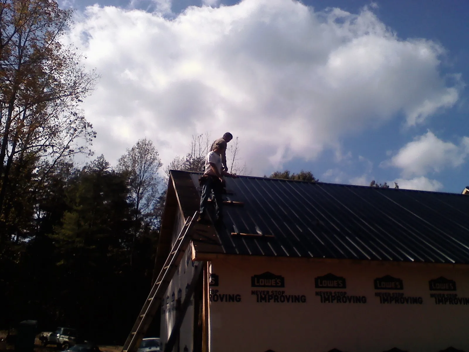 Roofer fastening dark metal panels high against a cloudy sky, from a Roof Inspection job in Wellpinit