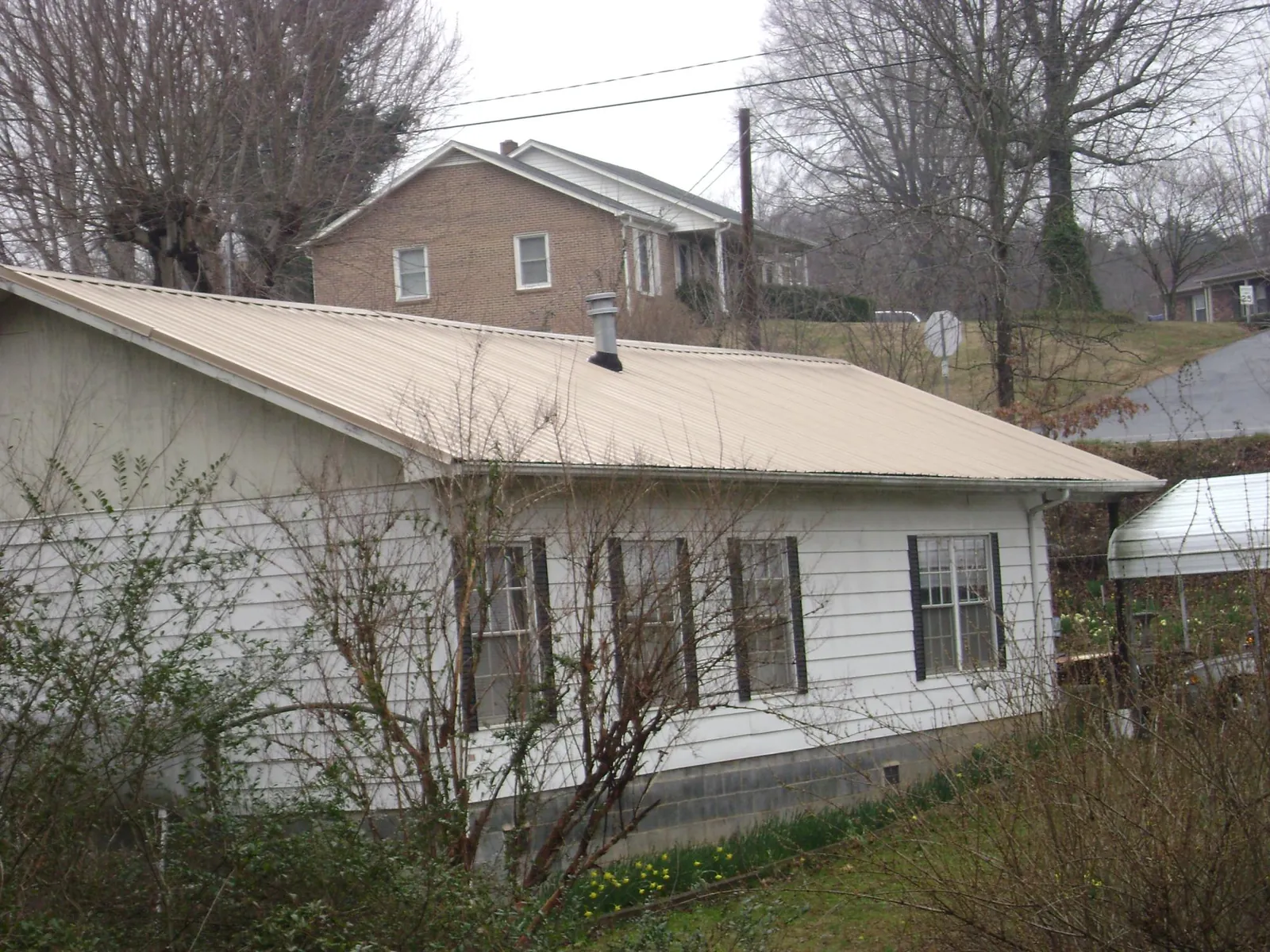 Tan metal roof on a white sided house set into a hillside — Commercial Roofing by Roofing Brothers in Wellpinit