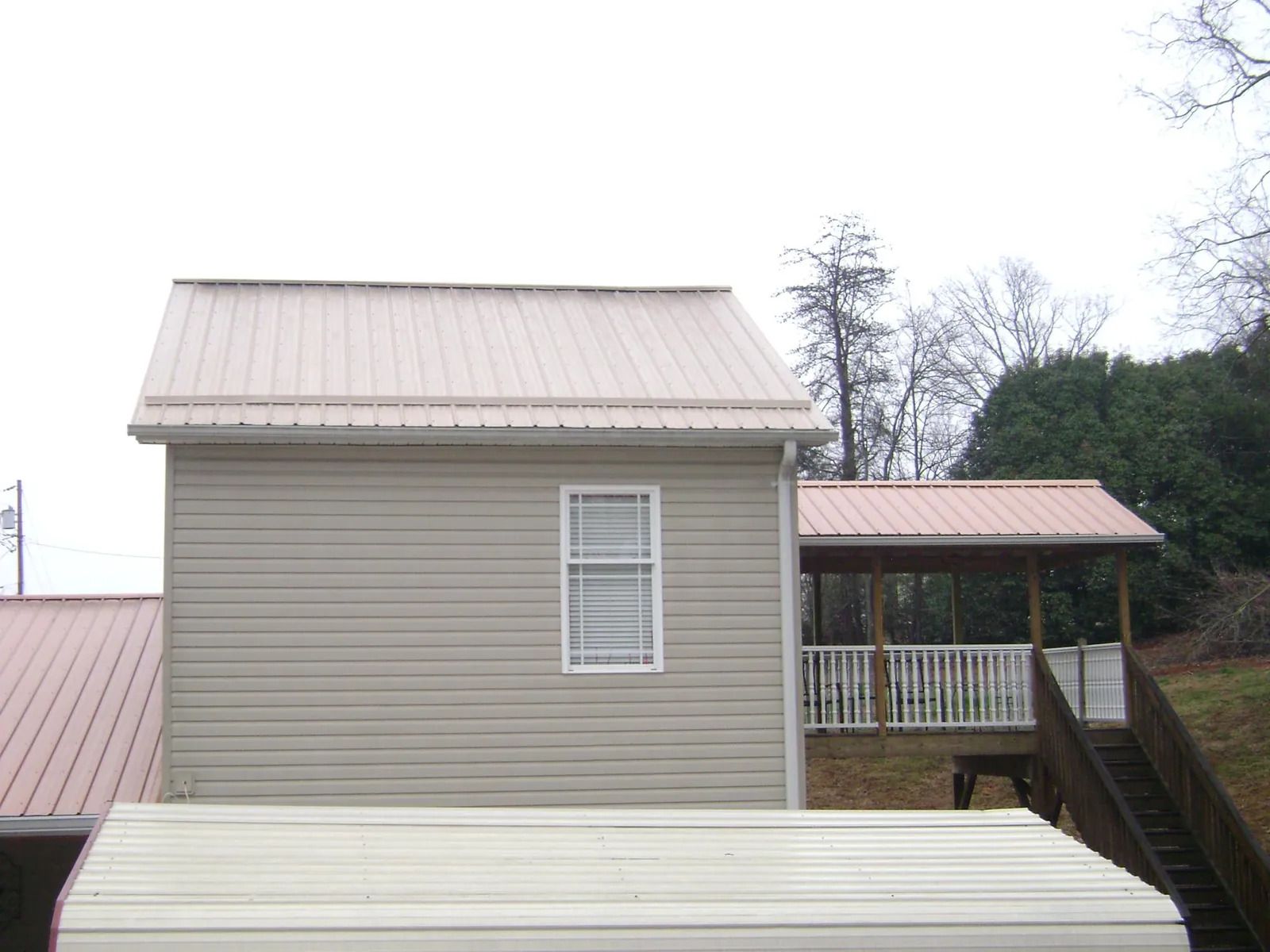 Tan metal roofs on a two story addition and attached porch, from a Roof Replacement job in Wellpinit